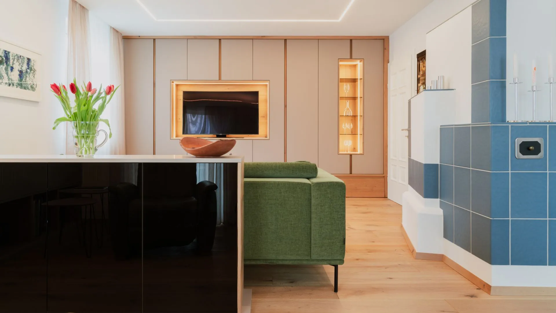 Offener Wohnraum mit schwarzem Sideboard, grünem Sofa und blau gefliestem Ofen