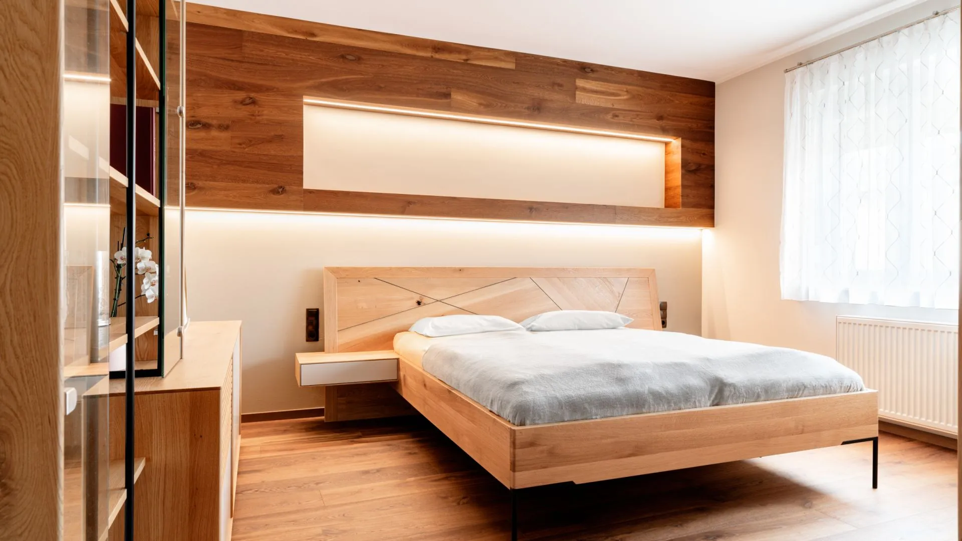 Schlafzimmer mit Holzbett, beleuchtetem Kopfteil und Spiegelschrank
