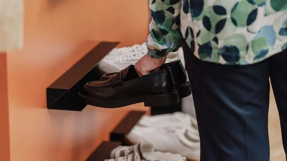 Person stellt Schuhe auf eine schwarze Wandablage