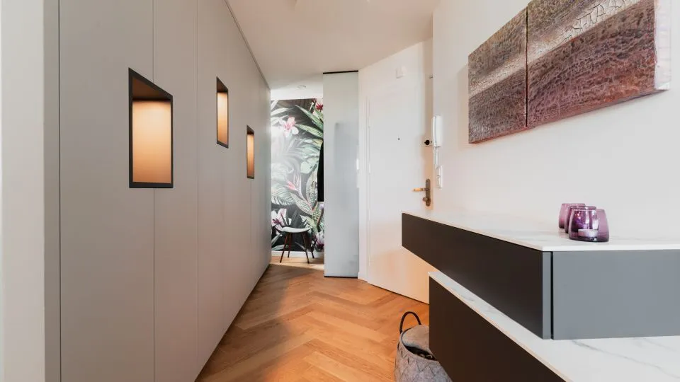 Gang mit beleuchteten Wandnischen, Sideboard und Fischgrätparkett