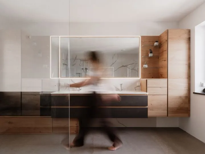 Badezimmer mit beleuchtetem Spiegel, Doppelwaschtisch und Holzwand