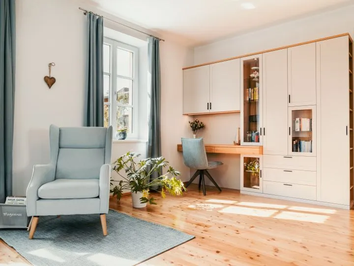 Wohnbereich mit Sessel, Schreibtisch am Fenster und weißem Einbauschrank