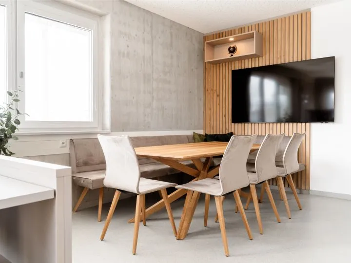 Esszimmer mit Holztisch, hellen Stühlen und Wandfernseher