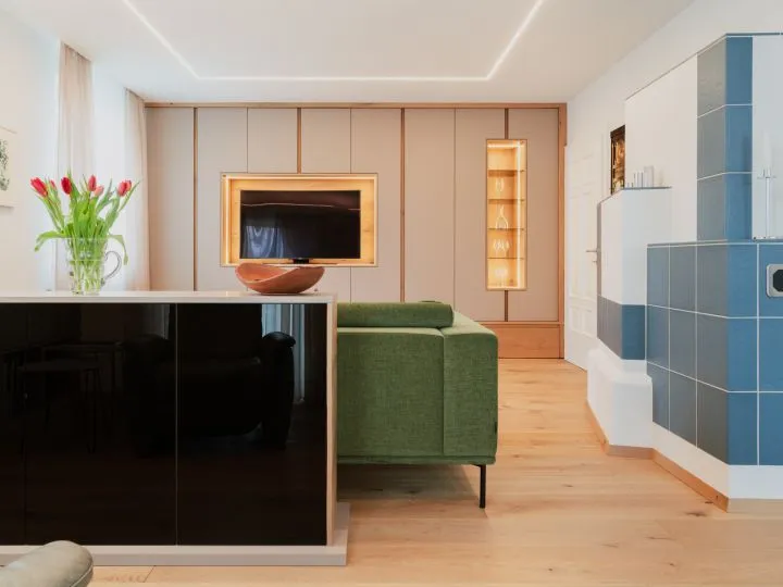 Offener Wohnraum mit schwarzem Sideboard, grünem Sofa und blau gefliestem Ofen