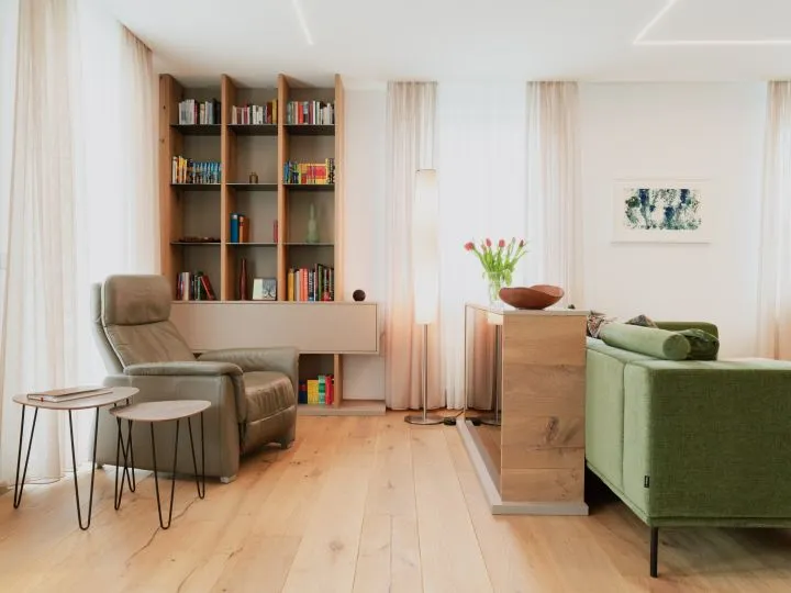 Wohnzimmer mit Bücherregal, Sesseln und grünem Sofa