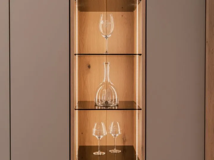 Beleuchtete Glasvitrine mit Karaffe zwischen matten Schrankfronten