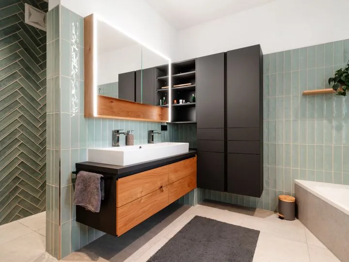 Badezimmer mit grünen Fischgrätfliesen, Holzwaschtisch und schwarzem Hochschrank