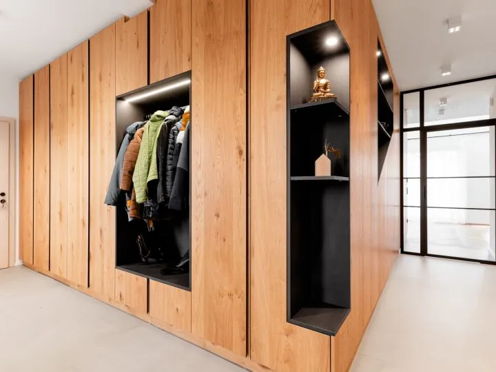 Offene Garderobe aus Holz mit Jacken und angrenzender Glastür