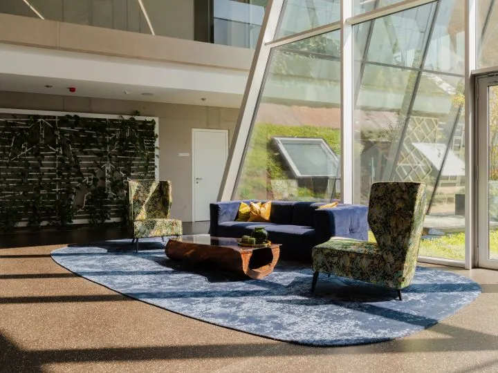 Loungebereich mit blauem Teppich, Sesseln und raumhoher Fensterfront