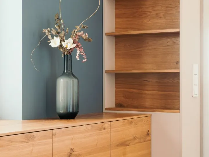Blaue Vase mit Trockenblumen vor einer Wandnische aus Holz