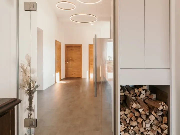 Flur mit Holztür und Blick in die angrenzenden Räume, daneben ein Brennholzstapel