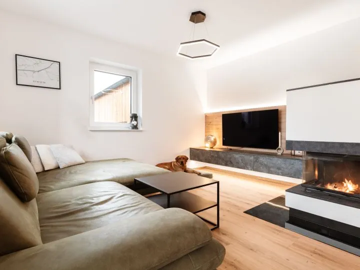 Wohnzimmer mit Ledersofa, Kamin und Fernseher auf einem Steinsockel