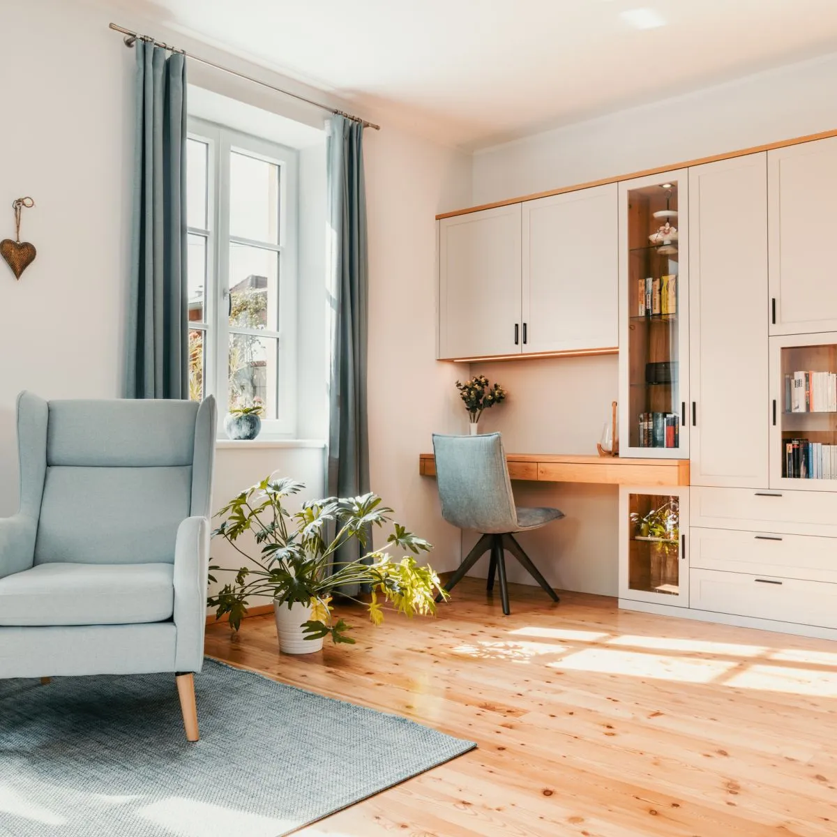 Wohnbereich mit Sessel, Schreibtisch am Fenster und weißem Einbauschrank