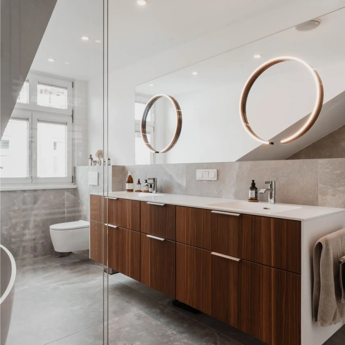 Badezimmer mit Doppelwaschtisch in Holz, zwei runden Spiegeln und Wänden in Steinoptik